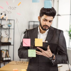 indian man working on tablet in front of office glass wall