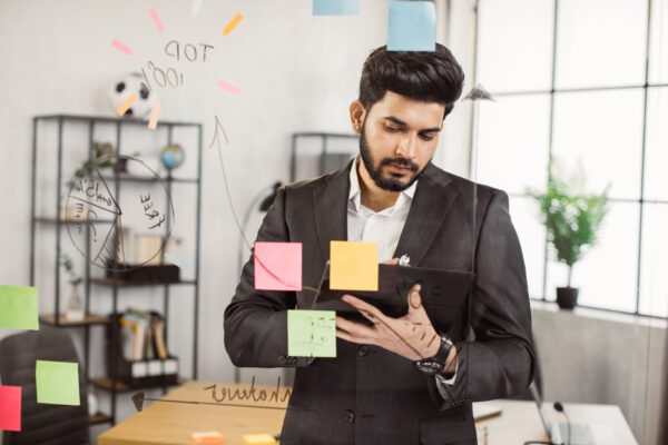 indian man working on tablet in front of office glass wall